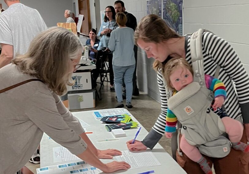 Primary Alex Romano Alex Romano signs in for the May 22 meeting on Winona County contaminated water, with her daughter Ruth, 7 months. (Photo by John Weiss)