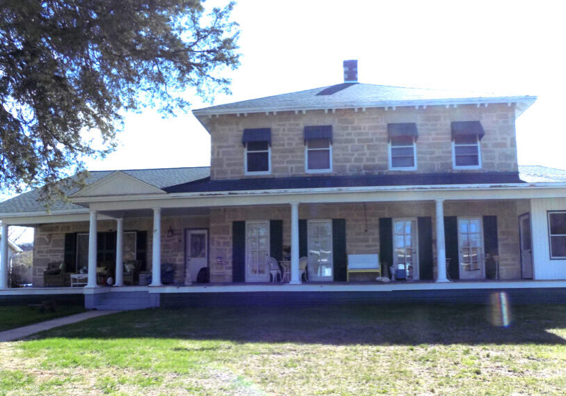 A large two-story tan brick home with a porch extending across the entire front.