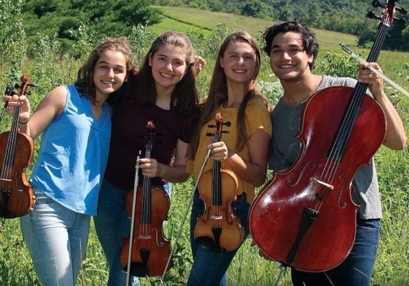 four youth musicians standing with instruments in outdoor setting