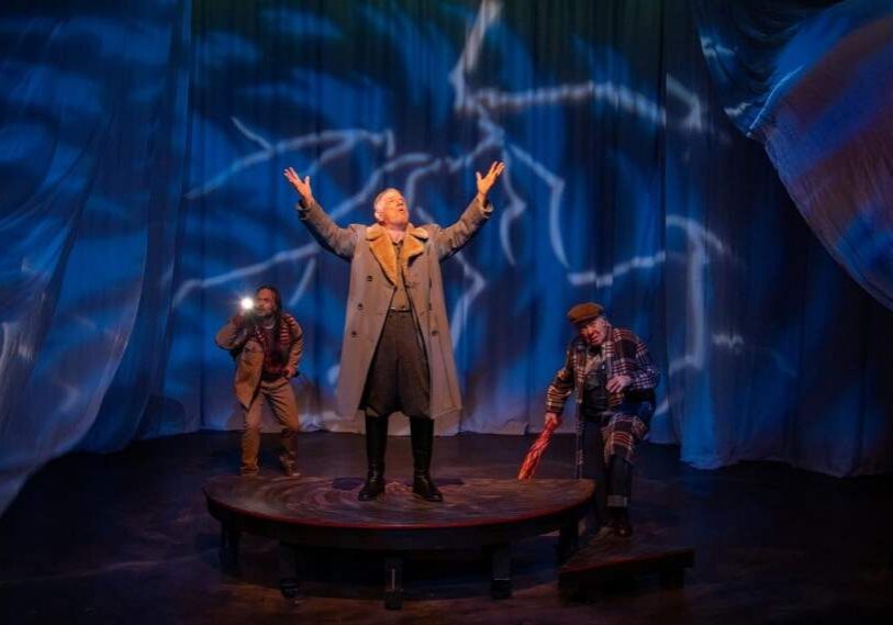 three actors on state with deep blue curtains in background